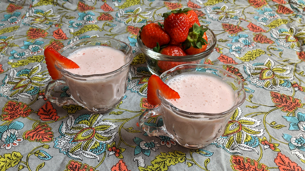 two small glass cups of pink milk punch garnished with strawberries