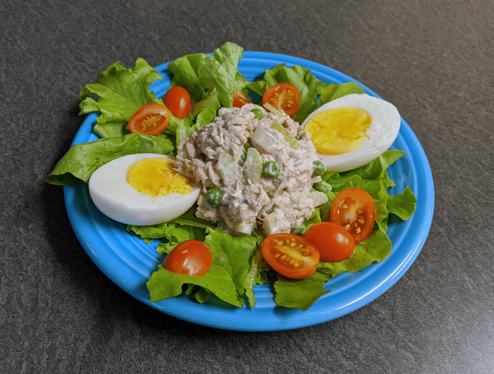 a scoop of tuna salad on a bed of leaves with egg and chopped tomato