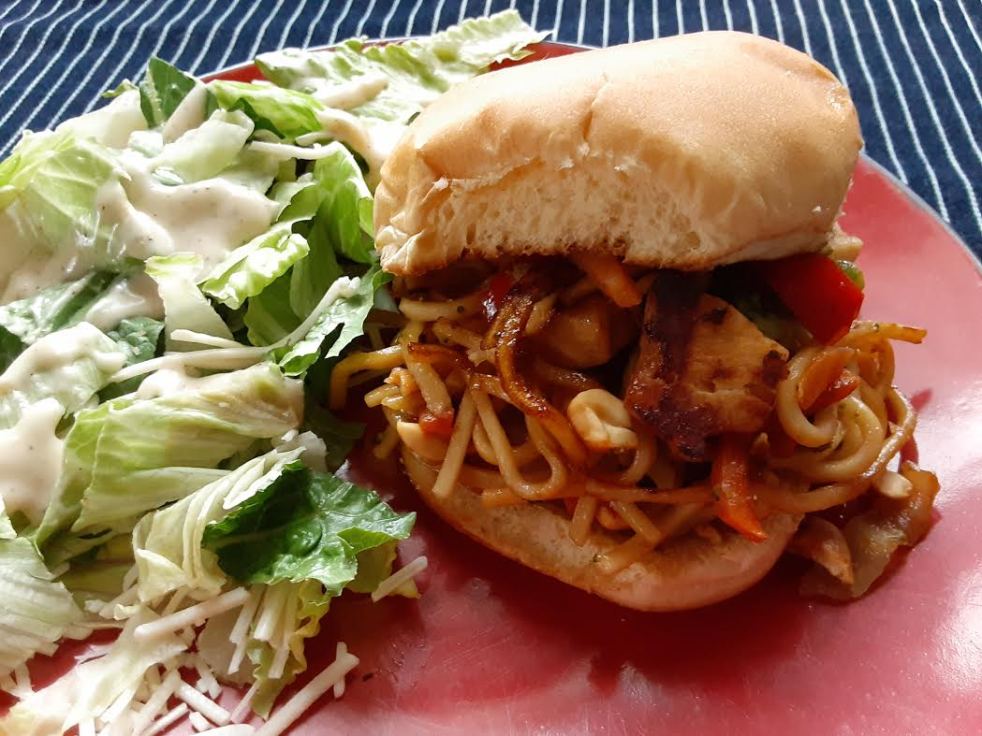 a chow mein sandwich on a red plate with a side salad