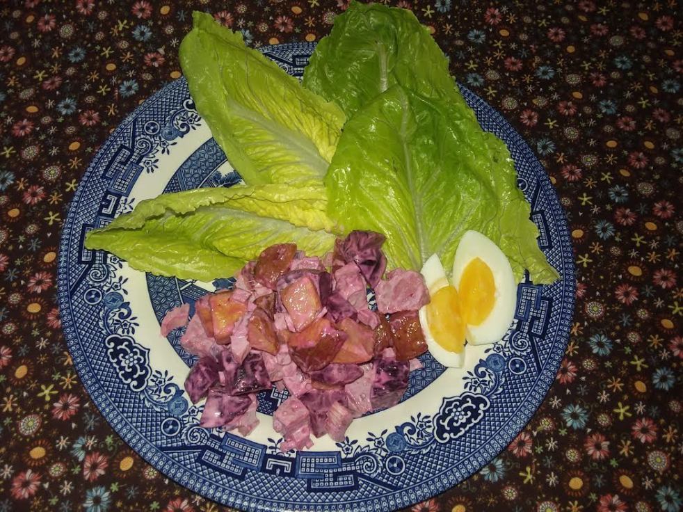 a helping of hashed corned beef salad on a blue plate with pieces of lettuce and slices of boiled egg
